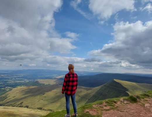 Back via of myself wearing a red check shirt and jeans overlooking the view from the top of Pen Y Fan in the Brecon Beacons.